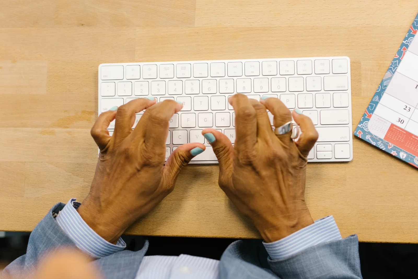 Hands typing on a sleek white keyboard over a wooden desk, showcasing professional work environment.