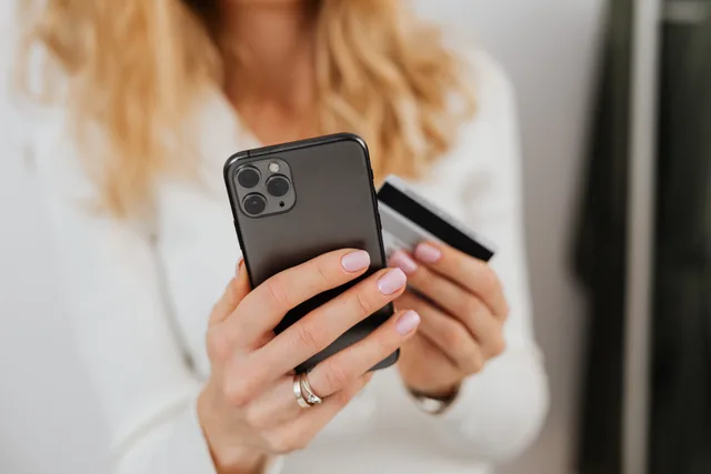 Close-up of woman holding smartphone and credit card for online transaction indoors. Mobile subscription and upgrade journeys